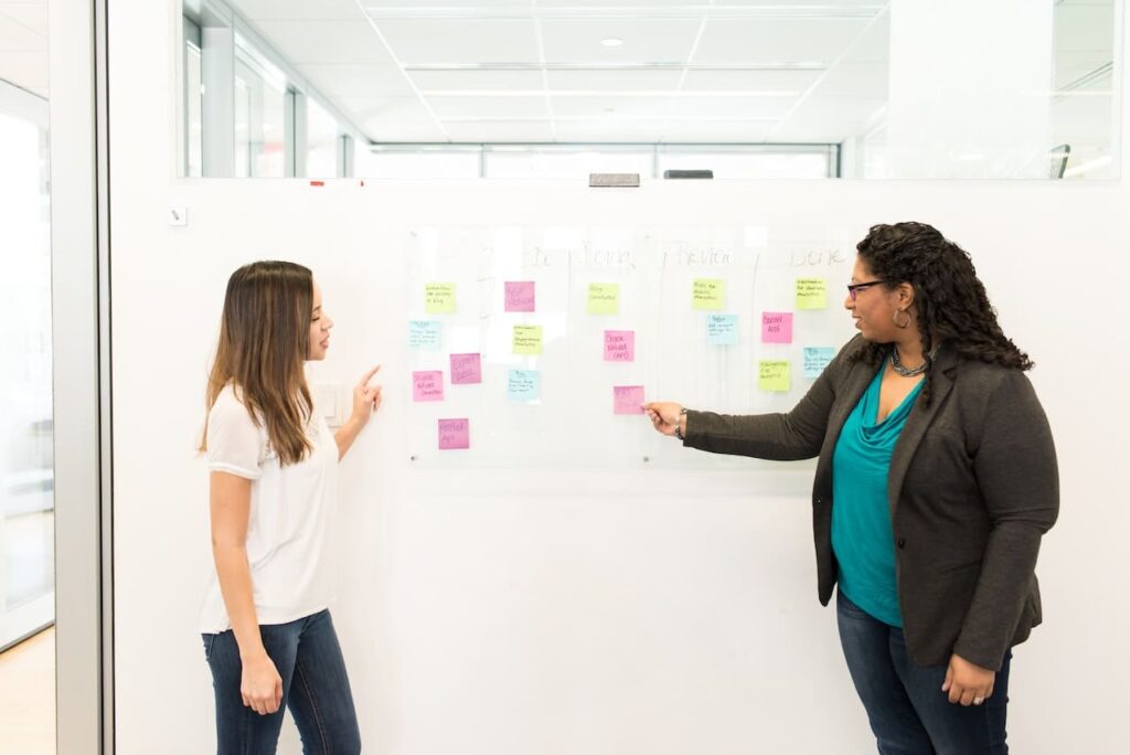 Dos mujeres trabajando frente a una pizarra con post its de colores.